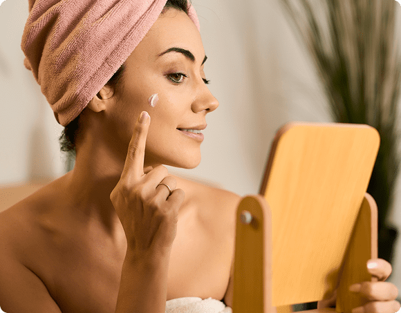 Person moisturizing face while looking in mirror